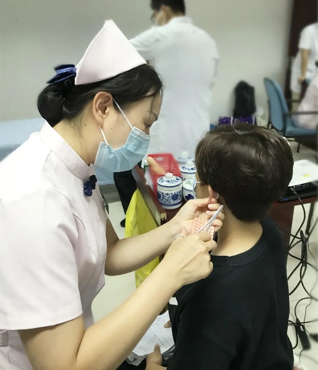 图为护理人员进行耳穴贴压治疗